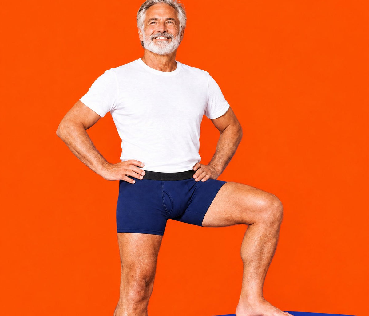 Silver-haired man in navy Dryden boxer briefs on an orange cube